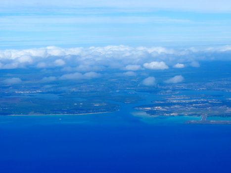 Aerial of Pearl Harbor and Honolulu Airport from the ocean with clouds over the island of Oahu, Hawaii.