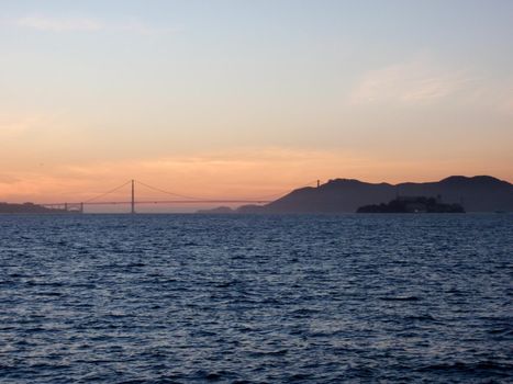 San Francisco city skyline, Golden Gate Bridge, and Alcatraz Island at dusk, seen from Treasure Island, with rolling waves and dramatic clouds in California.           