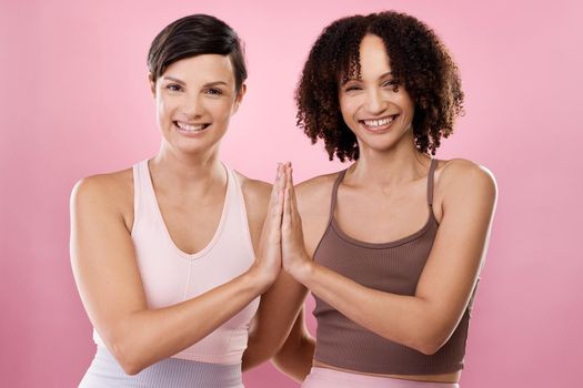 High fives for fitness. Cropped portrait of two attractive young female athletes meditating in studio against a pink background