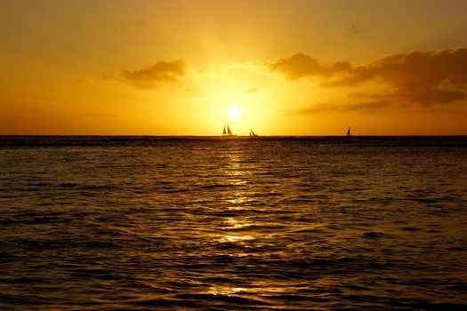 Sunset over sailing boats and reflecting on the Pacific ocean on the water off the coast of Oahu, Hawaii.