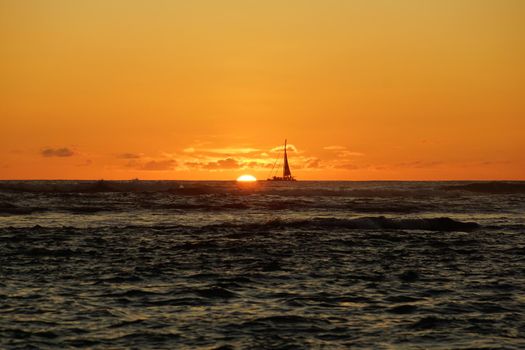 Sunset over the ocean with light reflecting on ocean waves moving with boats on the water in the distance off Waikiki with clouds on Oahu, Hawaii.