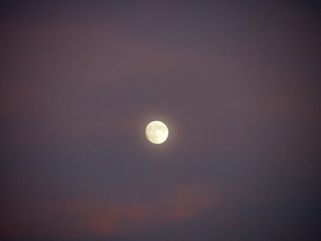 Almost full Moon in purple sky with a few clouds at dusk.