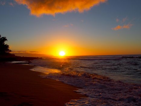 Beautiful Sunset over the ocean and beach with waves moving to shore and foot prints in the sand on the Sunset Beach on the North Shore of Oahu.    