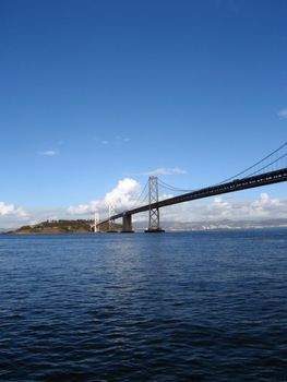 Cars cross the San Francisco side of Bay Bridge with Oakland in the distance on a clear day.