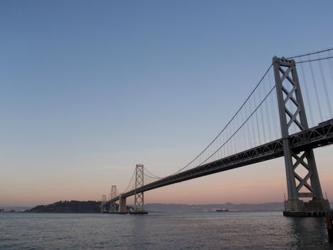 San Francisco side of Bay Bridge at dusk with Oakland in the distance on a clear day.