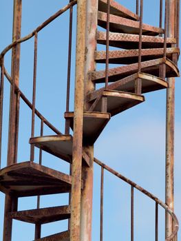 Old Rusted Metal Spiral Staircase against a blue sky.