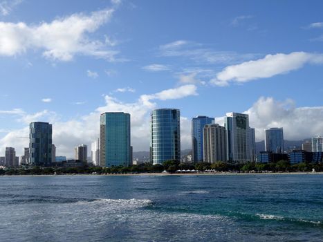 Waves roll towards Ala Moana Beach Park with office building and condos in the background during a beautiful day on the island of Oahu, Hawaii. 