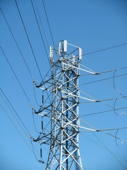 High Voltage Power Lines intersect at a large metal Utility pole with cell tower against a blue sky in San Jose, California.