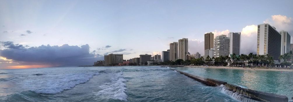 Waikiki - March 27: Panoramic of Waves rolling towards protected water of beach in world famous tourist area Waikiki at dusk with hotels in the distance.  