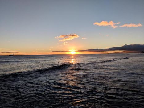 Dramatic Sunset through the clouds and reflecting on the Pacific ocean on the water with airplane flying off the coast of Oahu, Hawaii with Waianae Mountain range visible.  Shoot at Ala Moana Beach Park.