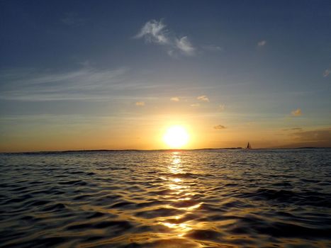 Sunset lowering to the ocean off Kaimana Beach with boats on the water on Oahu, Hawaii. 