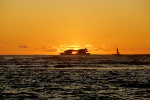 Sunset through the windows of a boat over the ocean with light reflecting on ocean waves moving with boats on the water in the distance off Waikiki with clouds on Oahu, Hawaii.