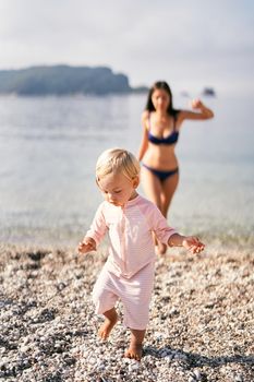 Little girl in a bathing suit walks barefoot on a pebbly beach. High quality photo