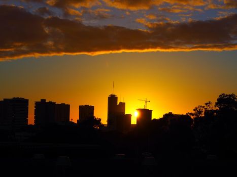 Honolulu Cityscape at Sunset with homes, skyscapers, cranes, temple, and Pacific ocean in view.