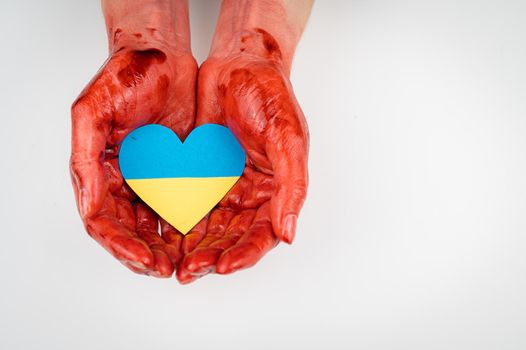 Woman with hands covered in blood holding a heart with the flag of ukraine on a white background