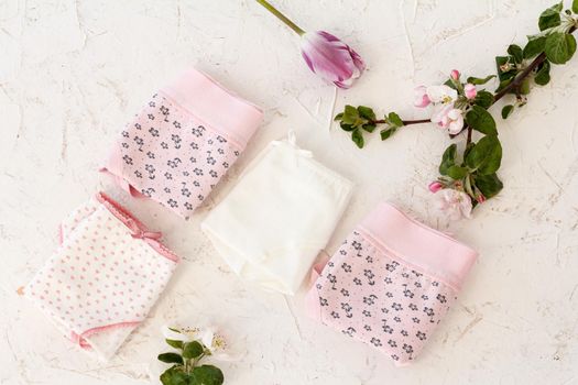 Folded cotton panties with a tulip and flowers of an apple tree on the white background. Woman underwear set. Top view.