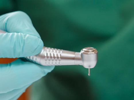 Dentist's hand in a mint latex glove with a new high-speed dental handpiece on the blurred background. Medical tools concept.