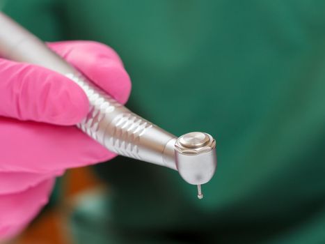 Dentist's hand in a pink latex glove with a new high-speed dental handpiece and a blurred green medical robe on the background. Medical tools concept.