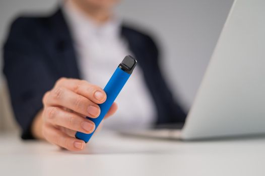 Business woman holding disposable vape while sitting at laptop