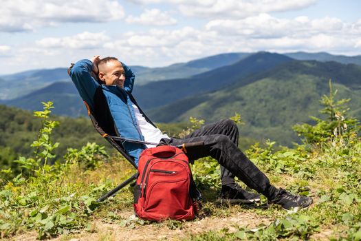 Guy tourist with a backpack stands in the mountains on a meadow with a backpack on his back.