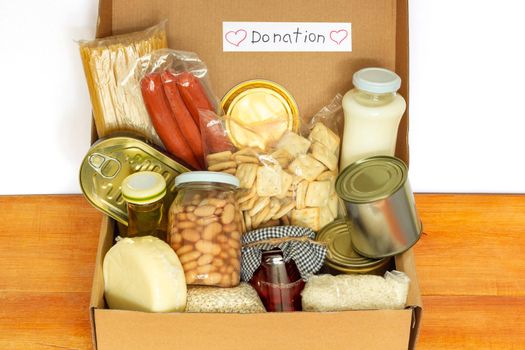 Set of grocery foodstaff for needy in crisis, pasta, beans, canned food, oil, milk, sausage, cheese in cardboard box ready for donation, top view