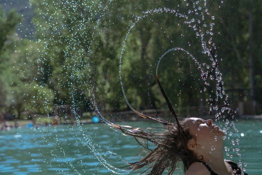 long-haired brunette girl in a black swimsuit shaking her hair in the water splash effect