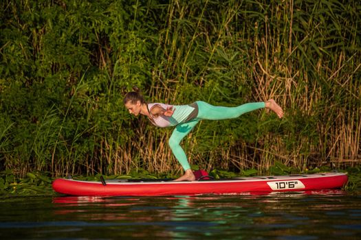 Young woman are doing yoga on a stand up paddle board SUP on a beautiful lake or river. The concept of a healthy lifestyle. Sport. Yoga. Hobby