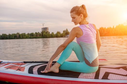 Young beautiful woman meditating in a sea at SUP paddleboarding. Healthy lifestyle. Girl in yoga pose relaxing in calm water.