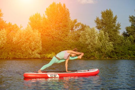 Young woman doing yoga on sup board with paddle. Yoga pose, side view - concept of harmony with the nature, free and healthy living, freelance, remote business.