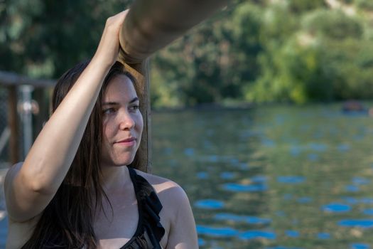 young attractive latin girl leaning on the trunk of a dock looking at the horizon, long brown hair and black swimsuit