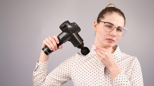 A caucasian woman uses a massager gun for pain in the muscles of her back and shoulders