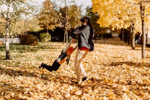 Father and son having fun in autumn park with fallen leaves, throwing up leaf. Child kid boy and his dad outdoors playing with maple leaves
