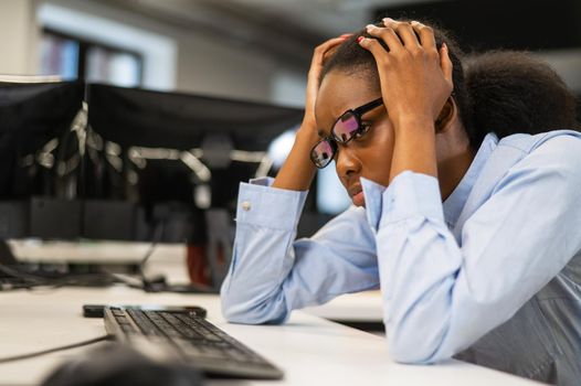 African young woman sitting at her desk clutching her head