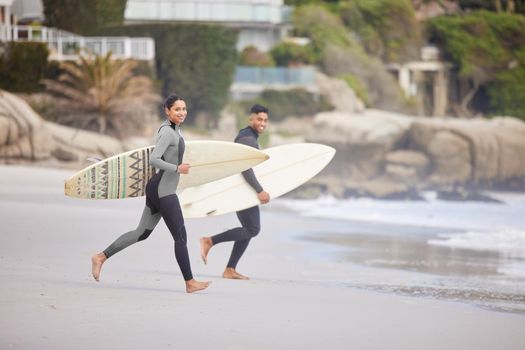 Lets go surfing. a young couple running into the water with surfboards at the beach