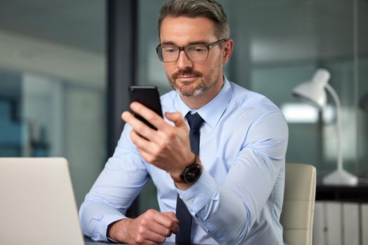 Communication simplifies everything. a handsome mature businessman sending a text while working at his desk in the office