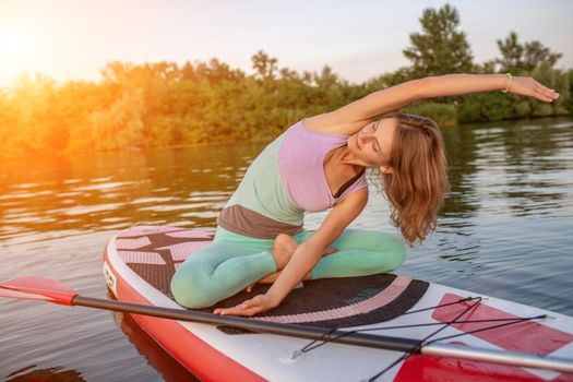 Young beautiful woman meditating in a sea at SUP paddleboarding. Healthy lifestyle. Girl in yoga pose relaxing in calm water.