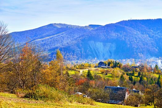 Autumn is one of the four temperate seasons. Outside the tropics, autumn marks the transition from summer to winter. Aerial view of an autumn small village in a valley and mountains in a blue haze