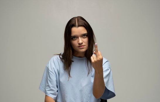 Portrait of crazy angry brunette woman wearing casual style beige t-shirt showing middle finger with one hand, rude gesture, face full of hatred and resentment