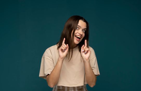 Beautiful young female emotional smiling and surprised looking at camera. Young woman with dark hair in beige t-shirt looking at camera with mouth open. Facial expressions, emotions, feelings