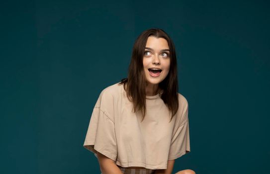 Young pretty brunette woman cute face expression posing in beige t-shirt on blue background isolated, emotional, funny