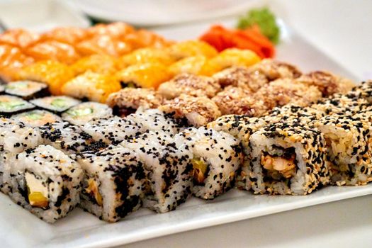 a Japanese dish consisting of small balls or rolls of vinegar-flavored cold cooked rice served with a garnish of raw fish, vegetables, or egg. Varied set of delicious oriental sushi lounge close up.