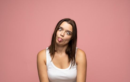 Brunette beautiful young woman standing over pink isolated background sticking tongue out happy with funny expression