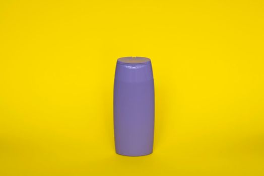 Violet plastic bottle of body care and beauty products. Studio photography of plastic bottle for shampoo, shower gel, creme isolated on yellow background