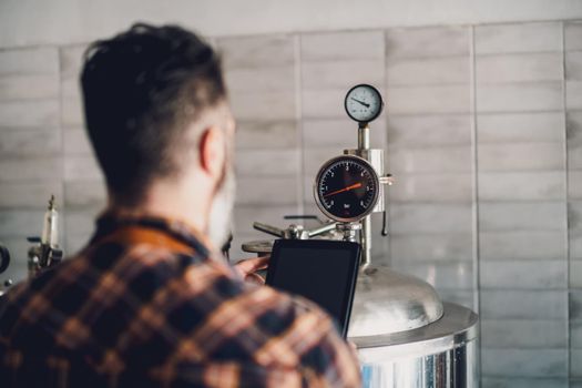 Man is working at craft beer factory. He is operating machinery in brewery. Small family business, production of craft beer.