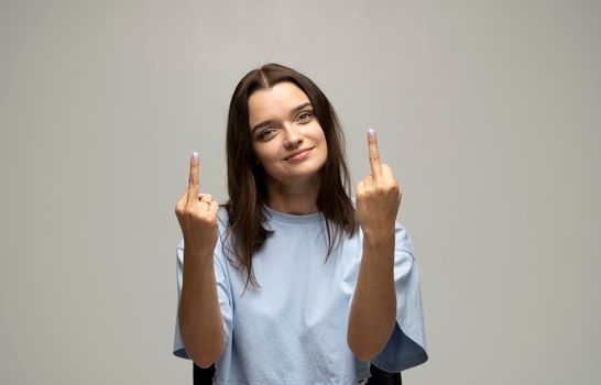 Beautiful brunette young woman wearing oversize blue t-shirt showing middle finger, provocation and rude attitude