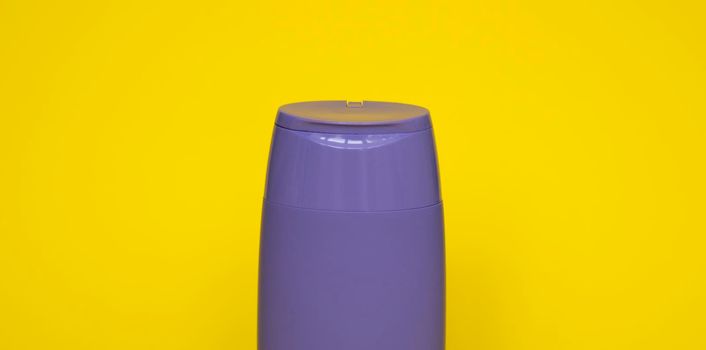 Violet plastic bottle of body care and beauty products. Studio photography of plastic bottle for shampoo, shower gel, creme isolated on yellow background