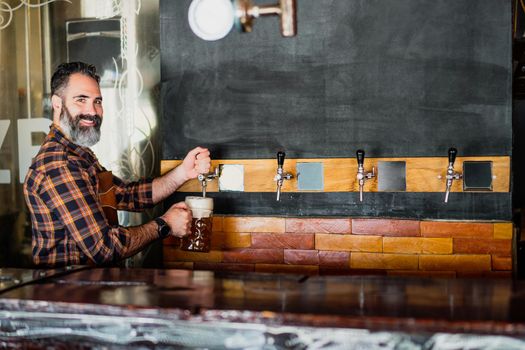 Portrait of barmen at pub. He pours beer into a beer glass. Blank space on table for you text or advert.