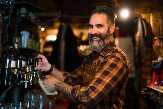 Portrait of cheerful barmen at pub. He pours beer into a beer glass.