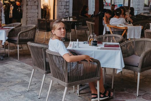 Girl Tourist Resting in the Ancient Narrow Street On A Beautiful Summer Day In MEDITERRANEAN MEDIEVAL CITY, OLD TOWN KOTOR, MONTENEGRO. Young Beautiful Cheerful Woman Walking On Old Street