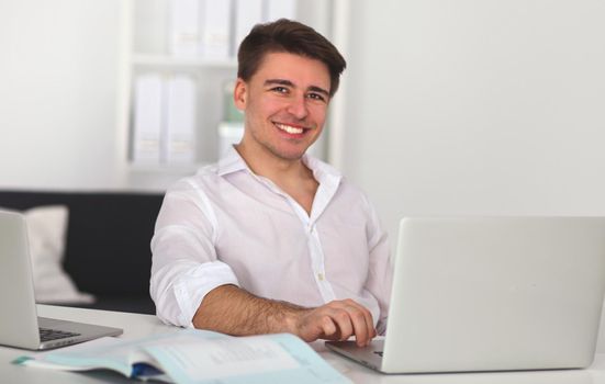 Young man sitting in chair and working on laptop computer .